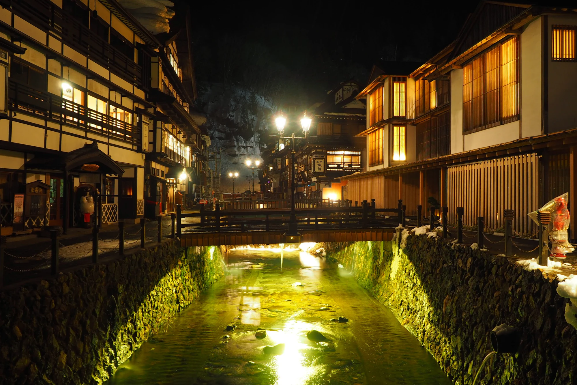 Vila termal japonesa iluminada à noite, com ryokans de madeira e rio ao centro