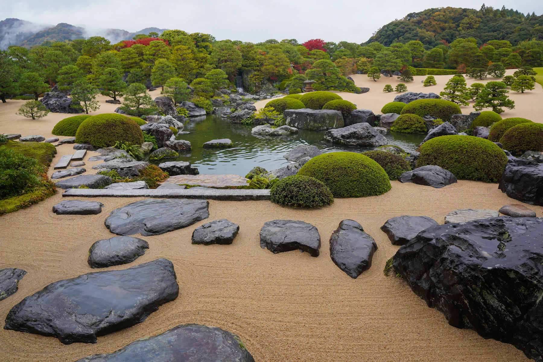 Jardim seco do Museu de Arte Adachi, com cascalho raked, pinheiros aparados e maples de outono ao fundo das montanhas