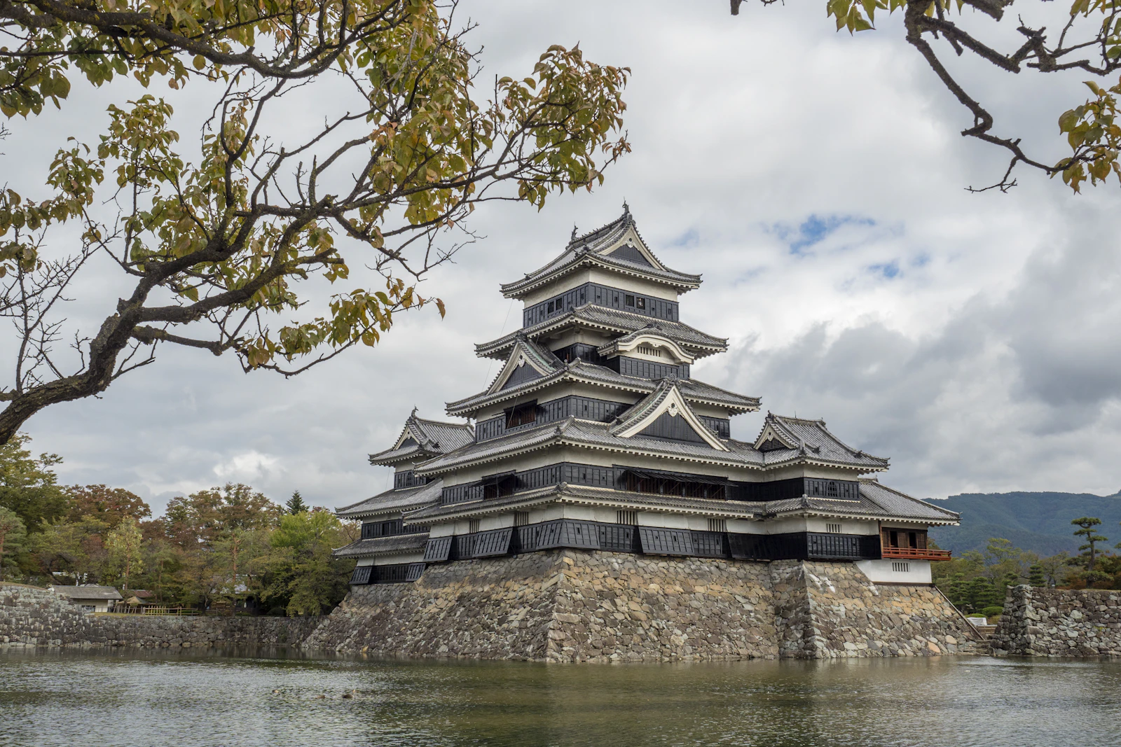 Castelo Negro de Matsumoto refletido no fosso, emoldurado por folhagem de outono